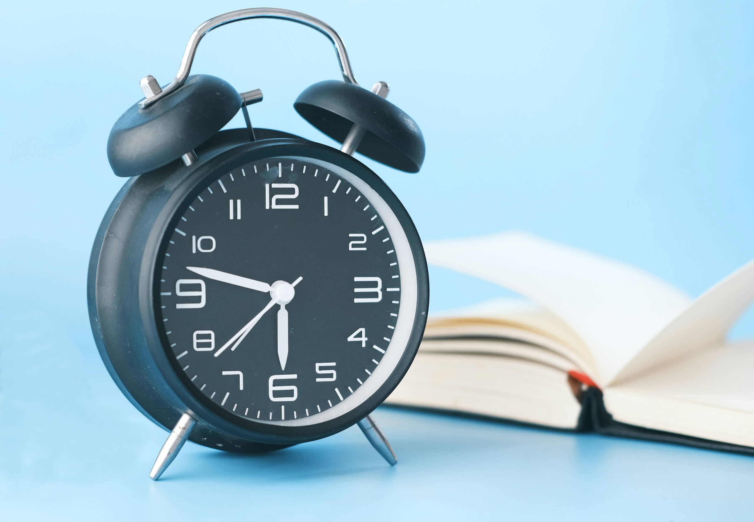 Wecker der 6:47 zeigt und ein offenes Buch im Hintergrund