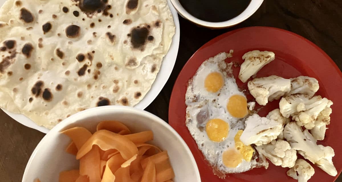 Frühstück mit einer Schale Karotten, einem Wrap, einem Teller mit Spiegel-Wachteleier und Blumenkohl